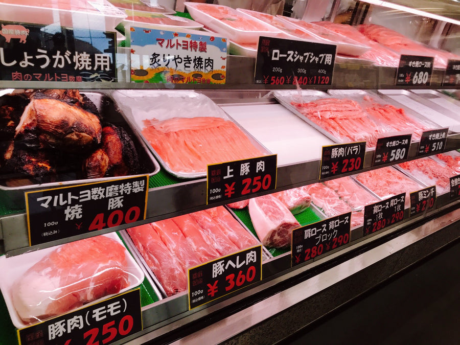 肉のマルトヨ 数磨のショーケース。豚肉や焼き豚が並び、品名と値段の札が立つ